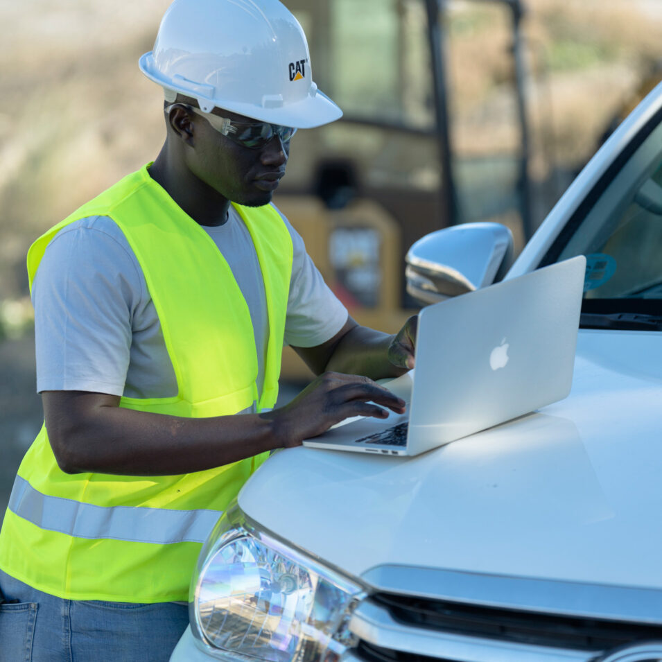 Man in safety gear using a laptop against the hood of a truck
