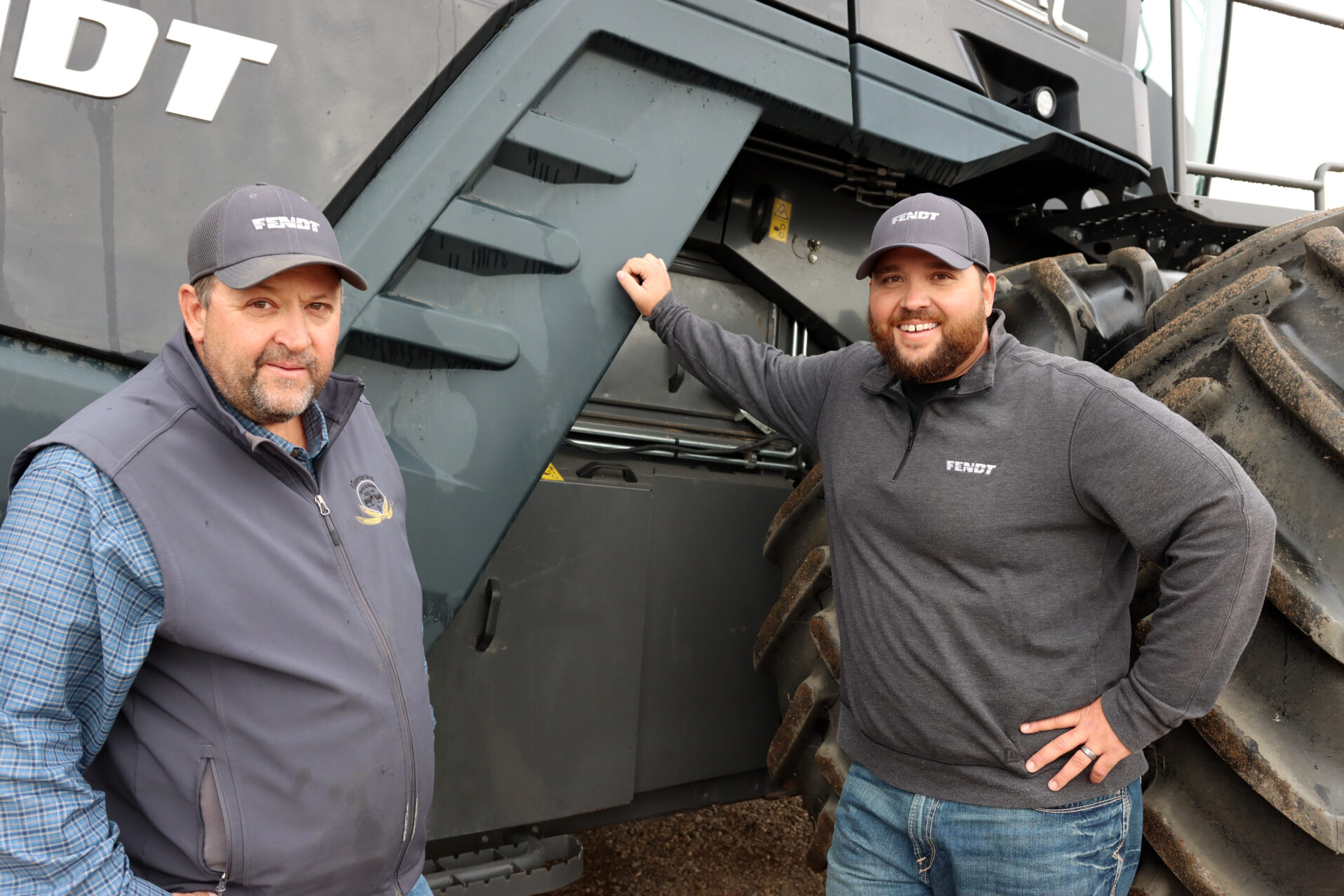Two men looking at the camera smiling next to equipment.