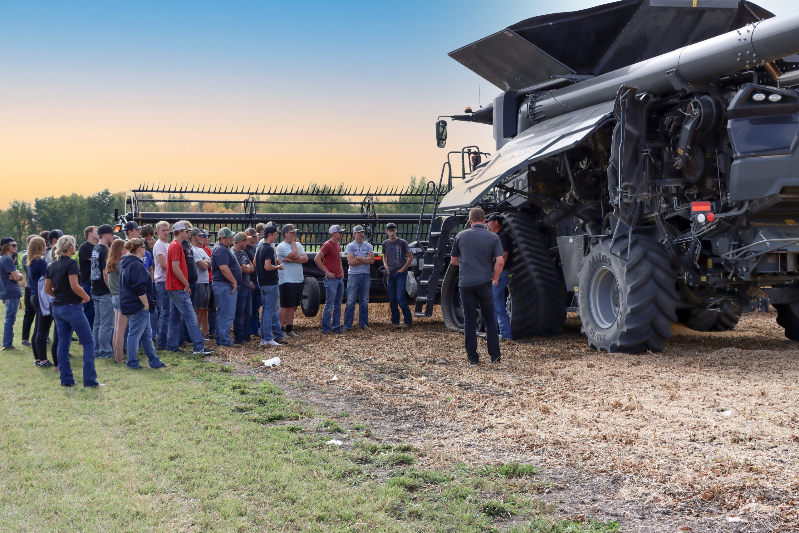 Group of students outside next to large field equipment.